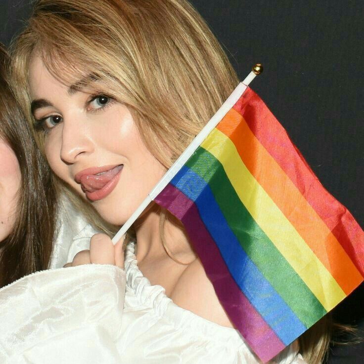 two beautiful young women standing next to each other holding a rainbow flag in their hands