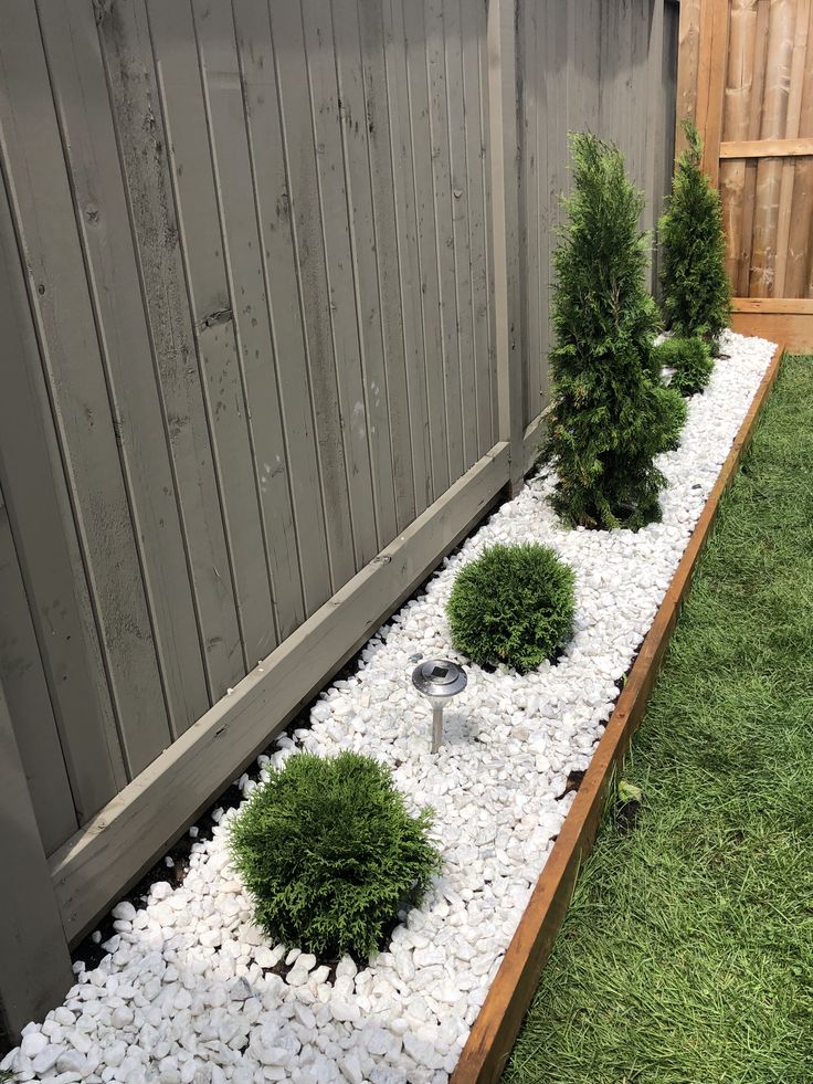 a small garden with gravel and rocks in the center, next to a wooden fence