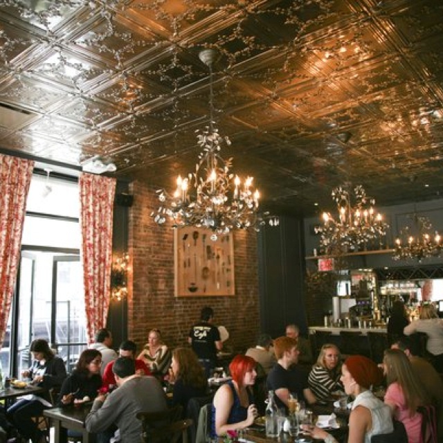 people sitting at tables in a restaurant with chandeliers hanging from the ceiling and windows