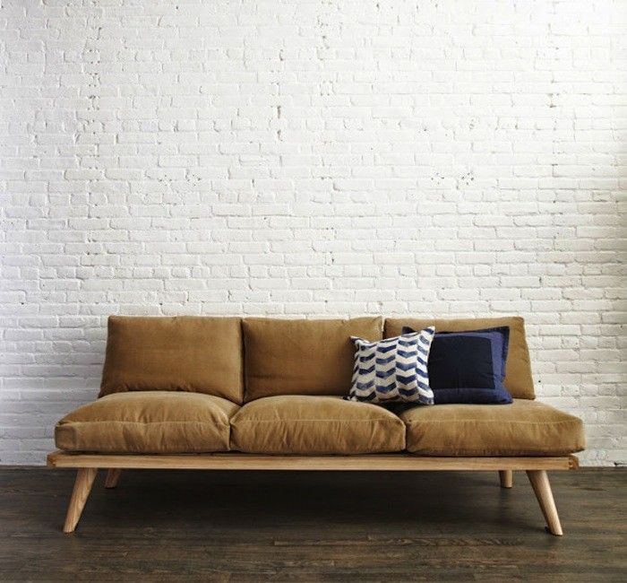 a couch with pillows on it in front of a white brick wall and wooden floor