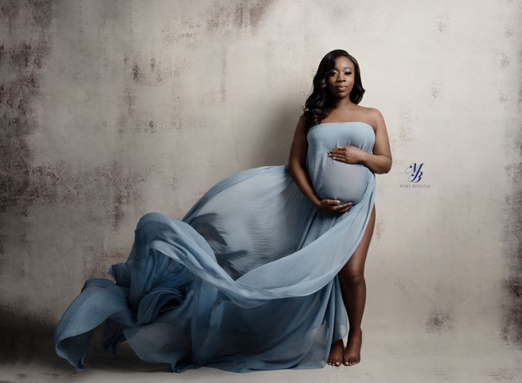 a pregnant woman in a blue dress poses for a photo with her hands on her belly