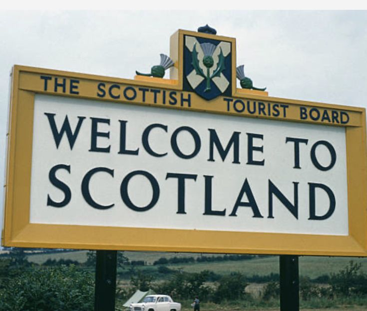 a welcome sign for the scottish tourist board in scotland, with a car driving by