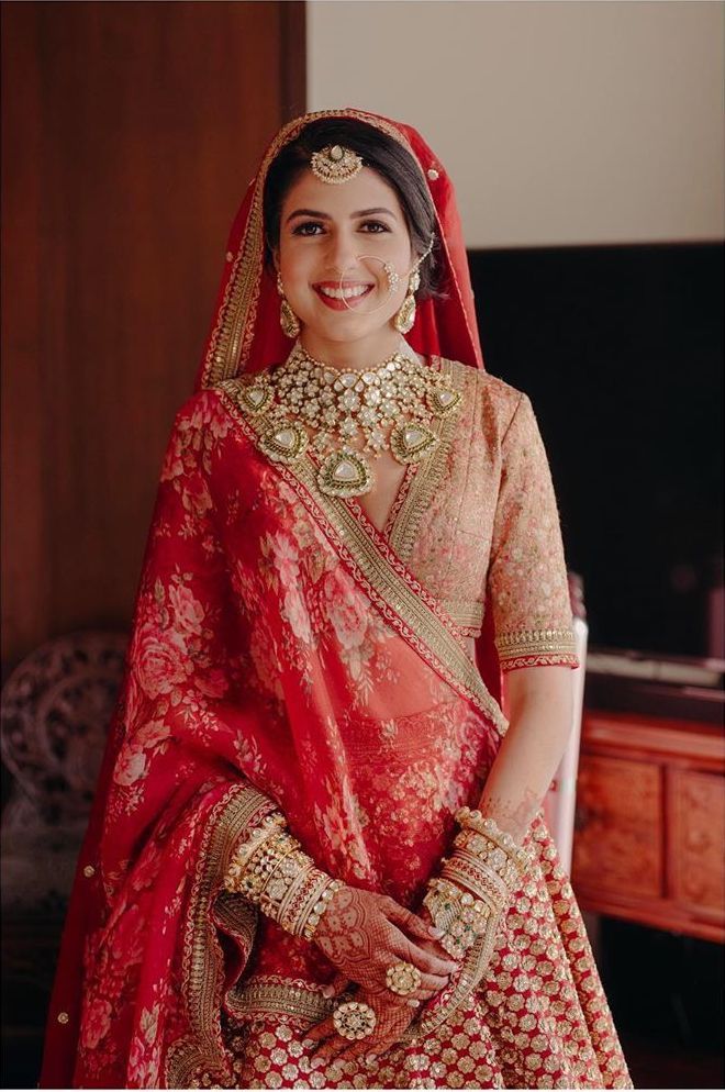 a woman in a red and gold bridal outfit posing for the camera with her hand on her hip