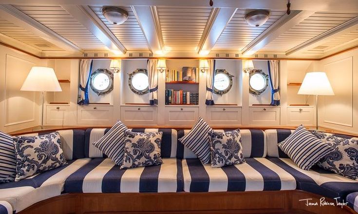 the inside of a boat with blue and white striped couches, pillows and lamps