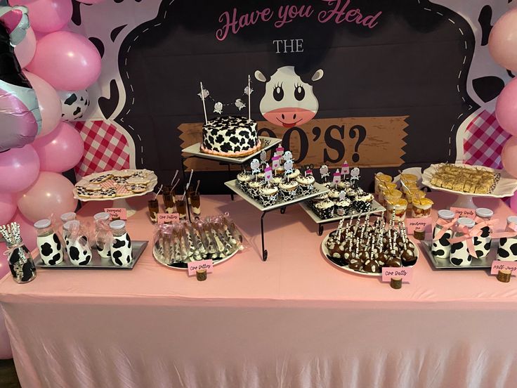 a pink table topped with lots of desserts and balloons in the shape of cows