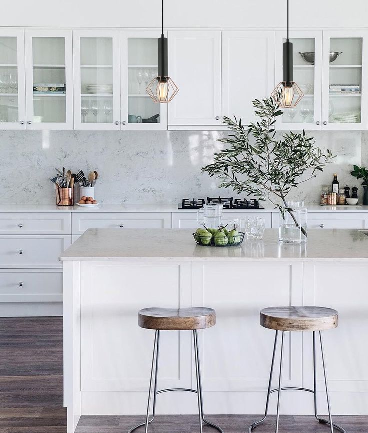 two stools sit at the center of a kitchen island with white cabinets and marble countertops