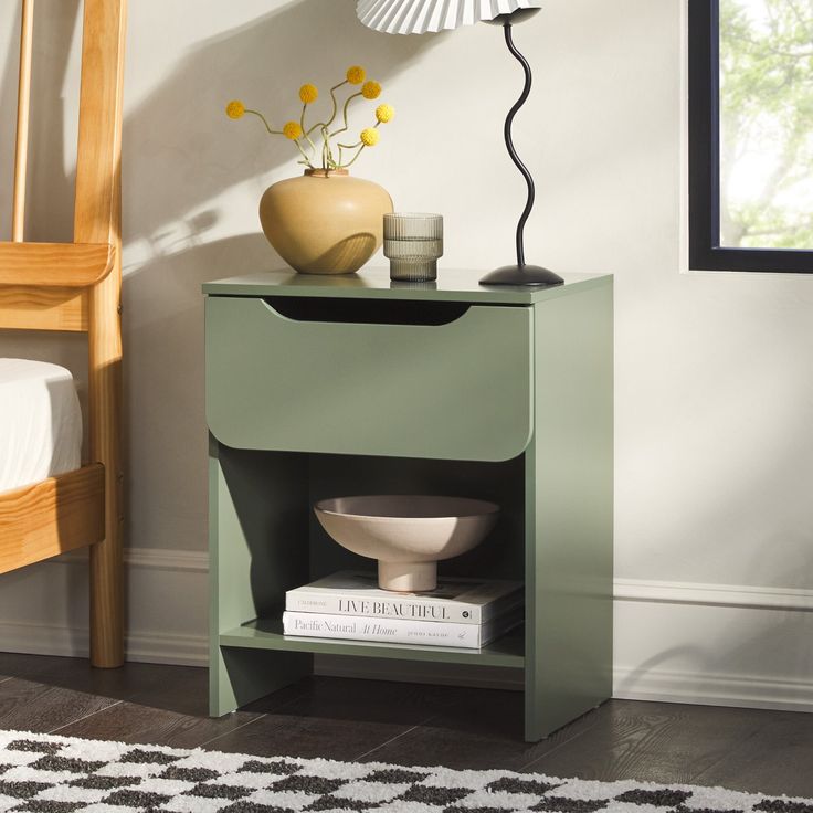 a nightstand with a lamp, vase and books on it