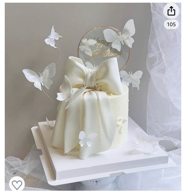 a white wedding cake decorated with butterflies and a bow on top is sitting on a table