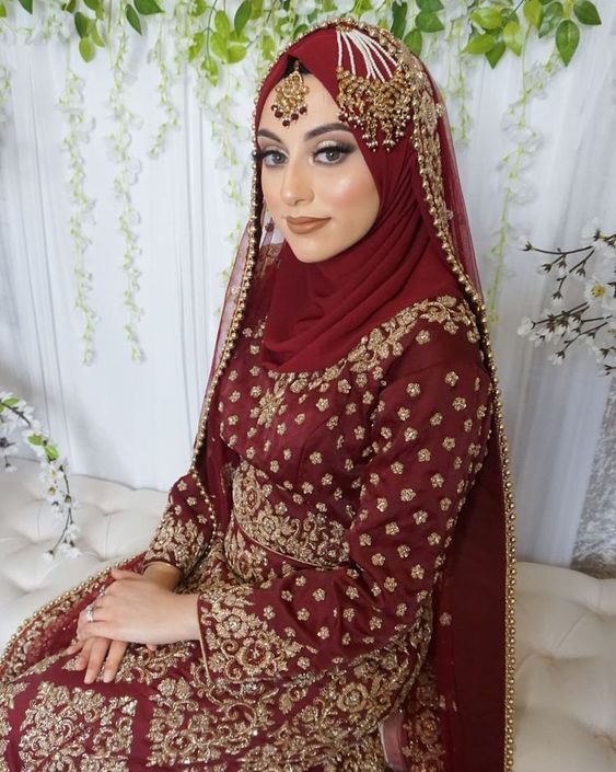 a woman in a red and gold bridal outfit sitting on a white couch with greenery behind her