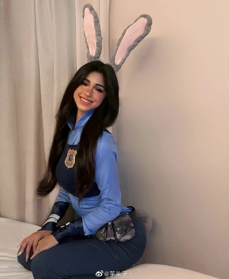 a woman sitting on top of a white bed in a blue shirt and bunny ears