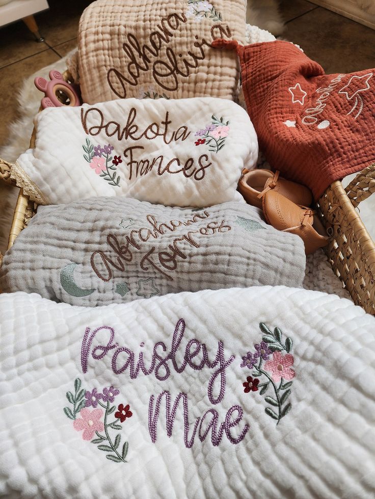 three personalized blankets with embroidered names are on the floor in front of a basket