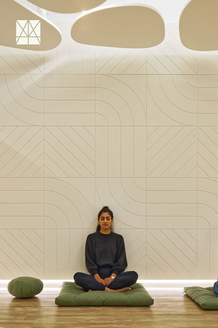 a woman sitting on top of a green mat in front of a wall with circles