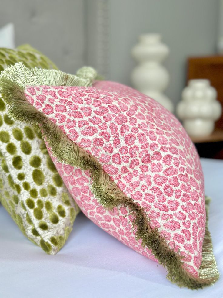 two decorative pillows sitting on top of a white bed covered in pink and green fabric