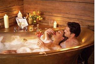 a man and woman taking a bath in a large tub with candles on the side