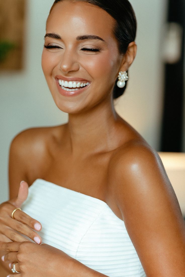 a woman in a white dress smiling and holding her hands together