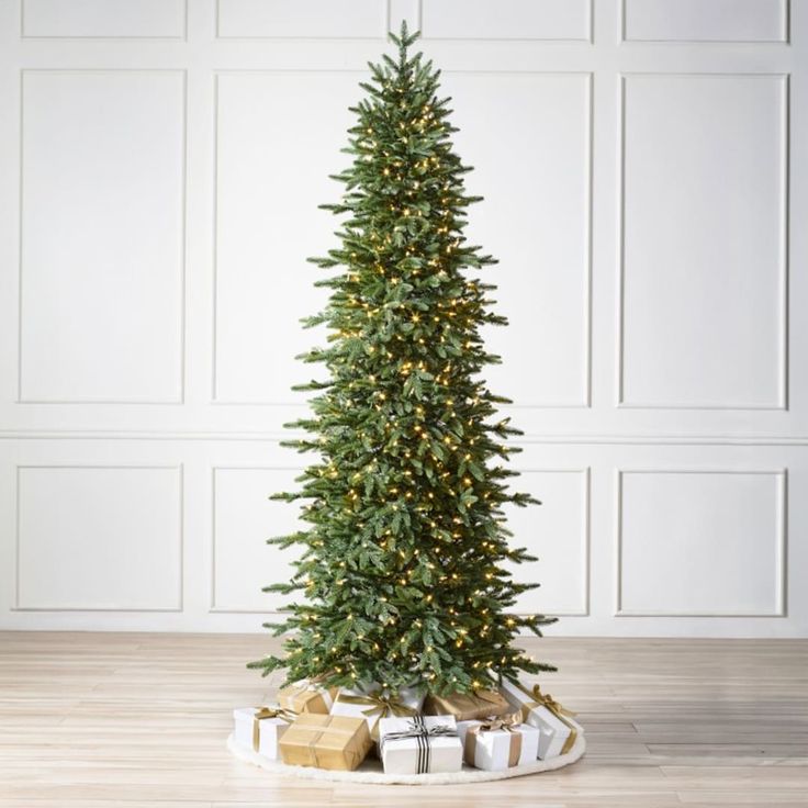 a christmas tree with presents under it on a wooden floor in front of a white wall