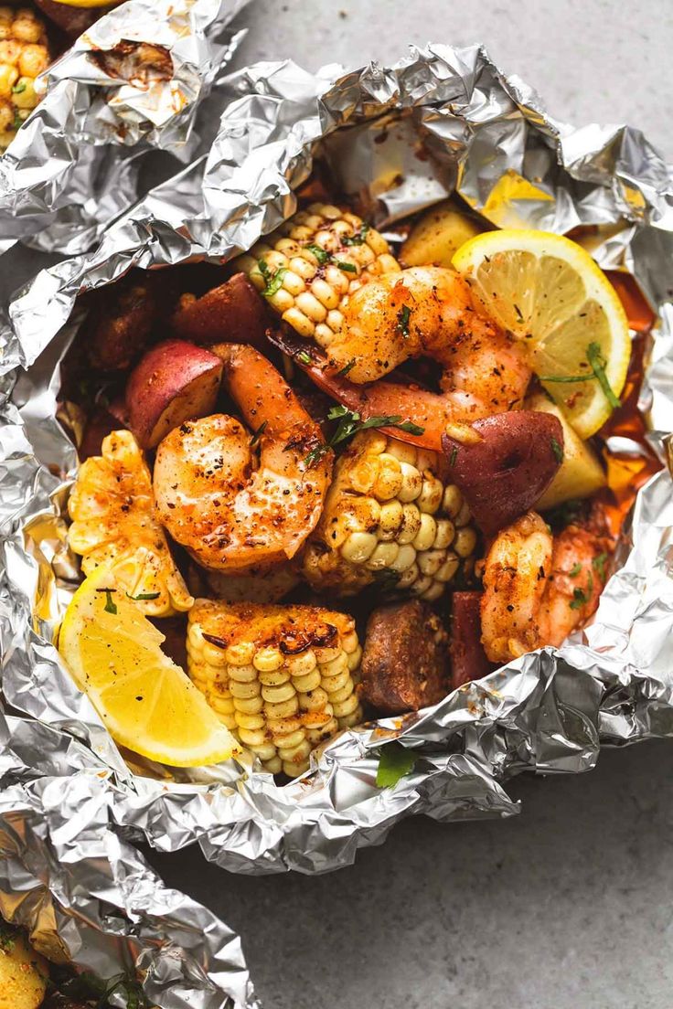 grilled shrimp and corn on the cob in foil with lemon wedges, parsley