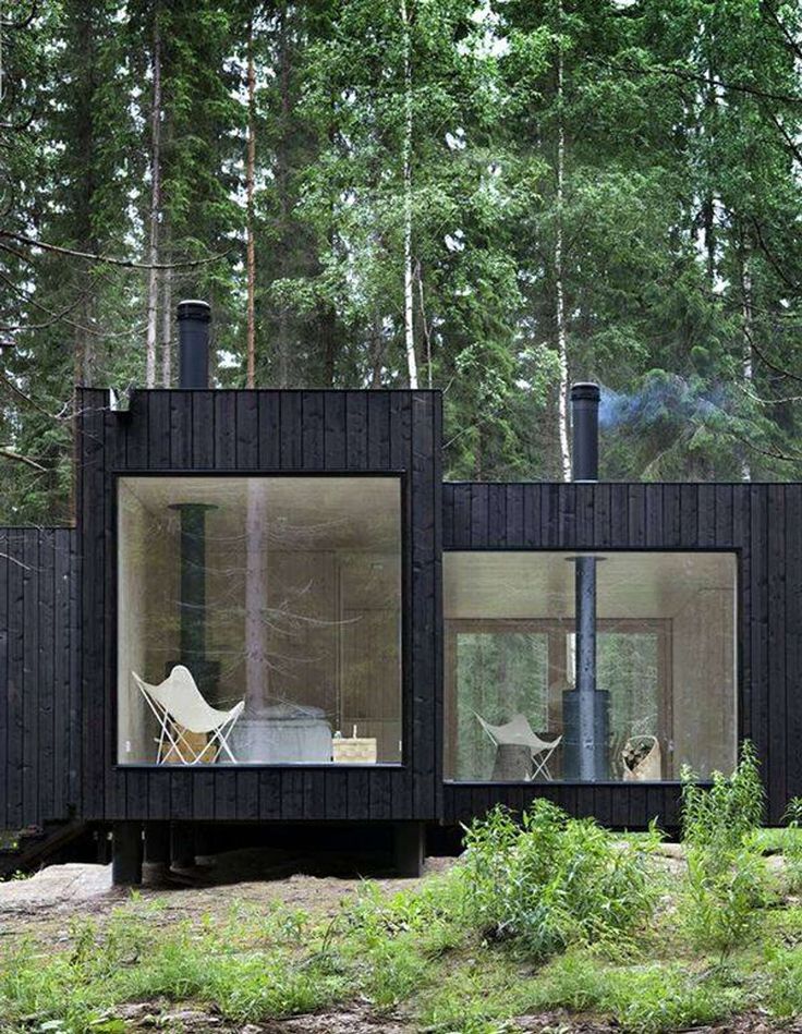 a small cabin in the middle of a forest with two chairs and a table inside