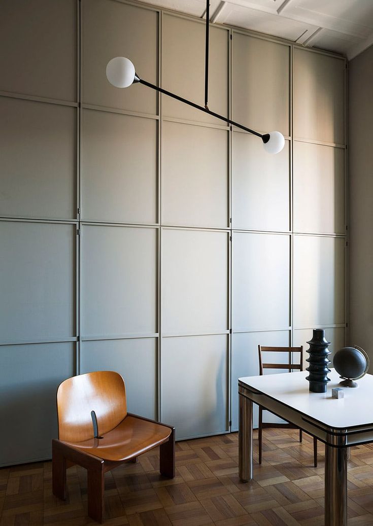 a room with a table, chair and lamp on the wall in front of it