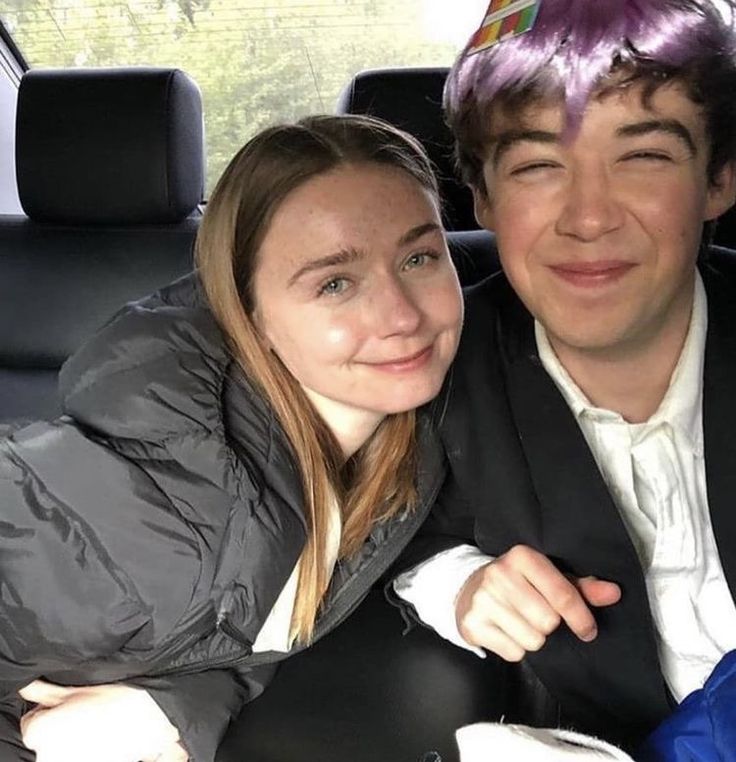 a young man and woman sitting in the back seat of a car smiling at the camera