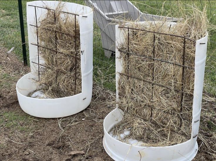 two white containers filled with hay sitting in the grass