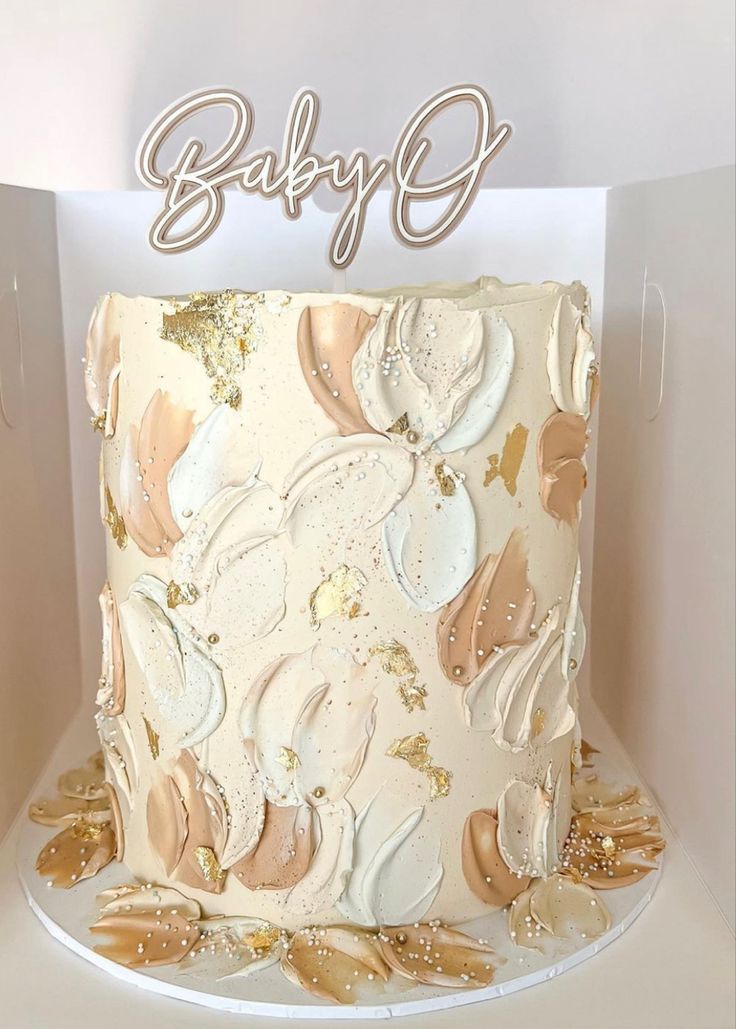 a white cake with gold leaf decorations and the word baby g on top is sitting in a box