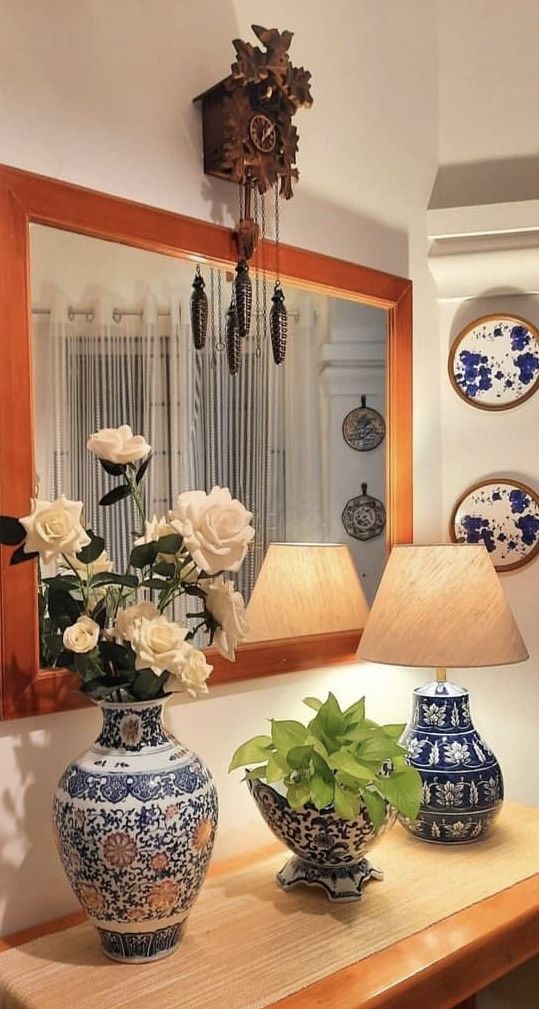 two vases with flowers sit on a table in front of a mirror and lamp