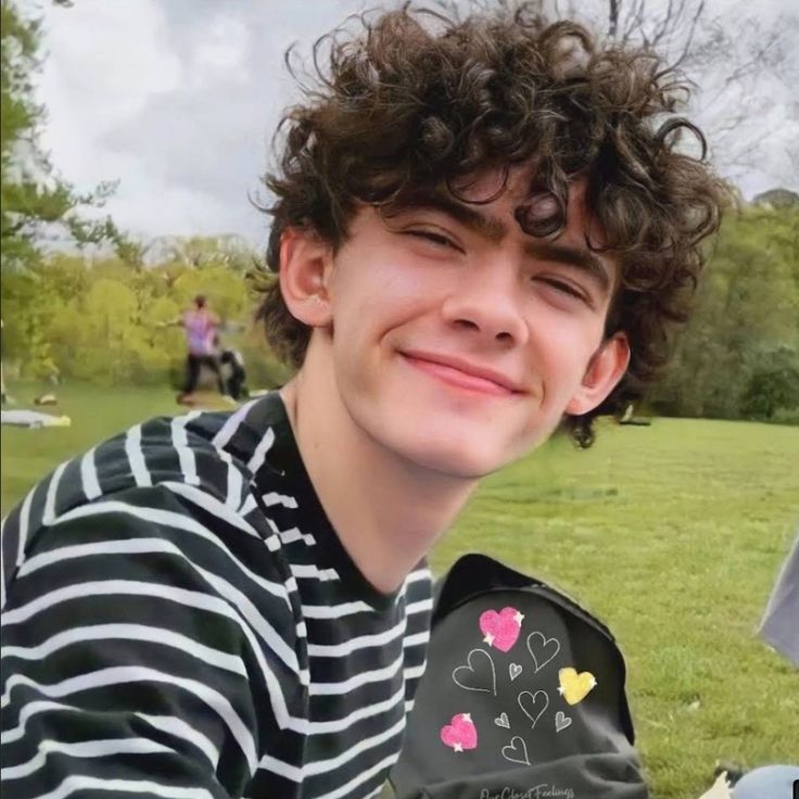 a boy with curly hair is smiling at the camera while holding an object in his hand