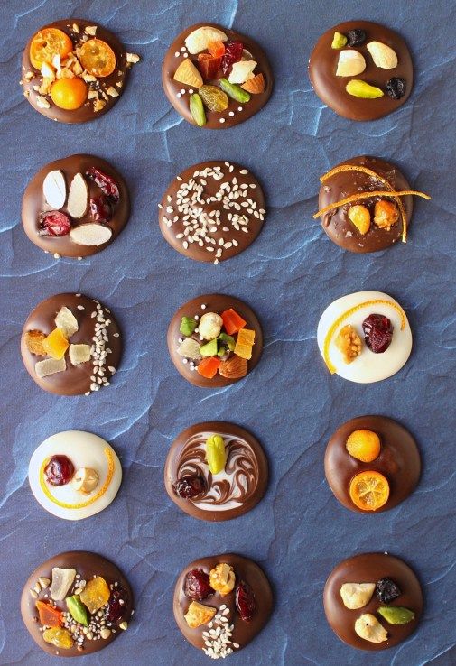 chocolate donuts with different toppings are arranged on a blue tablecloth and laid out in rows