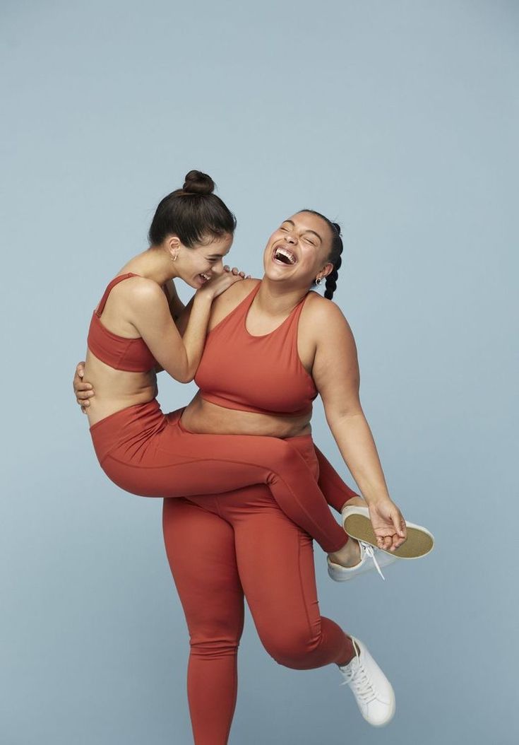 two women in sports wear are laughing and holding each other's back while posing for the camera