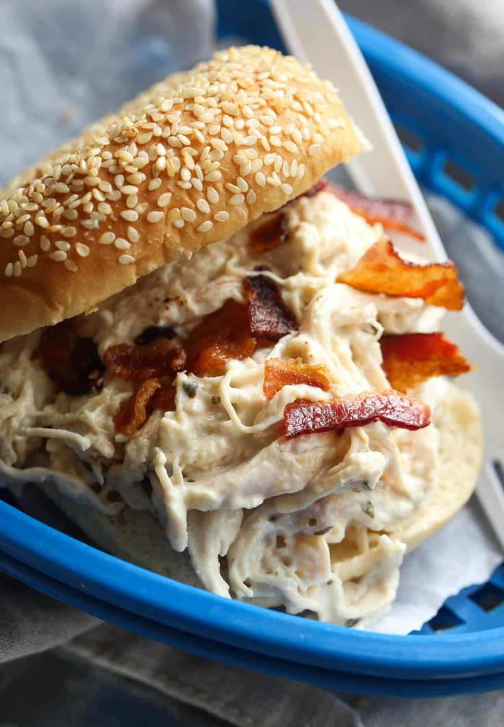 a chicken salad sandwich with bacon and sesame seeds in a blue bowl on a table