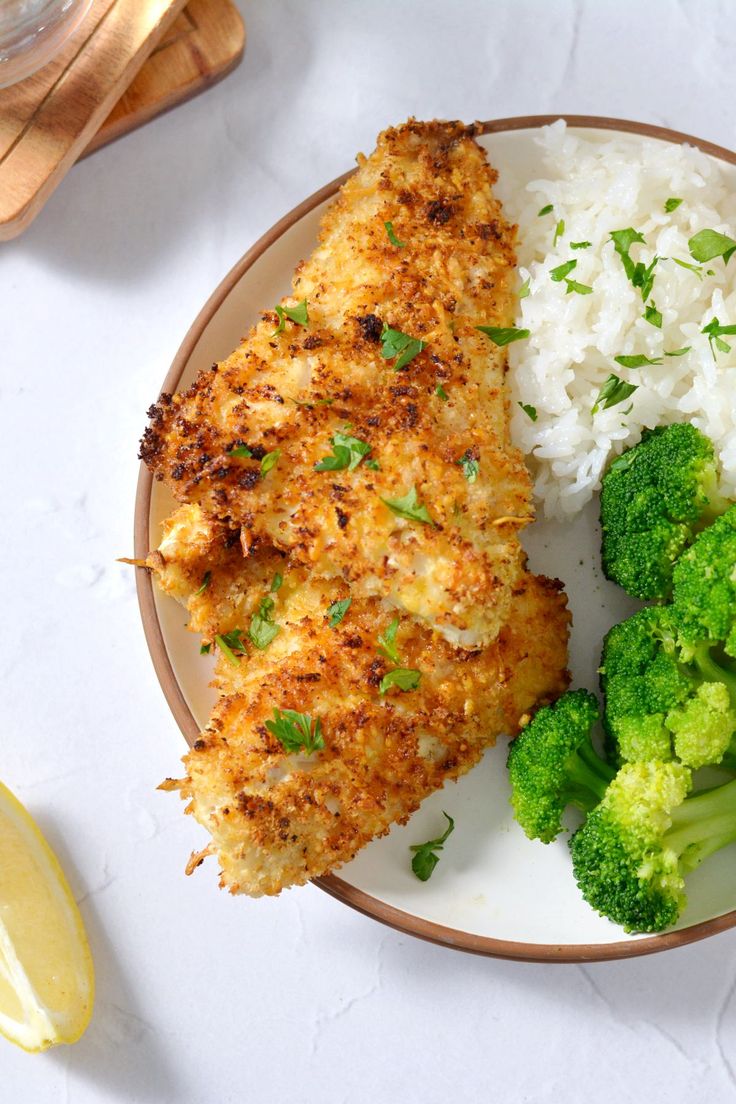 a plate with chicken, rice and broccoli on it next to a lemon wedge