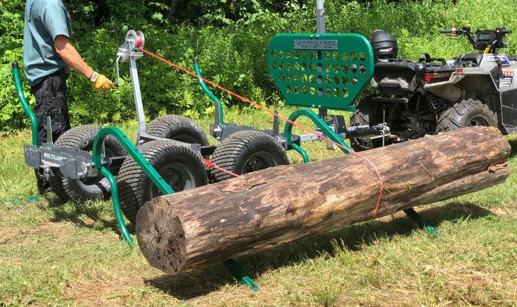 a man standing next to a large log on top of a grass covered field with an atv behind it