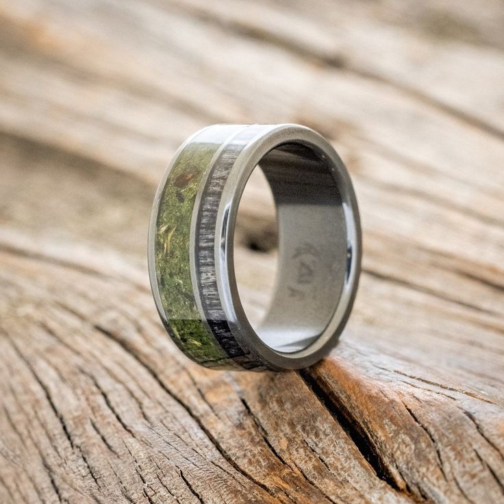 a wedding ring with moss inlays on it sitting on a piece of wood