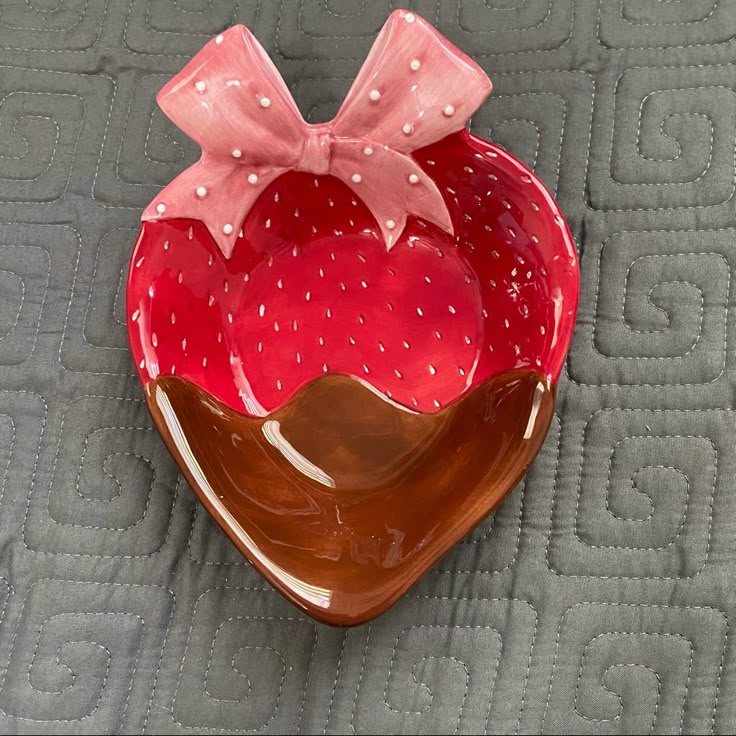 a strawberry shaped bowl with a pink bow on the top and brown base, sitting on a quilted surface