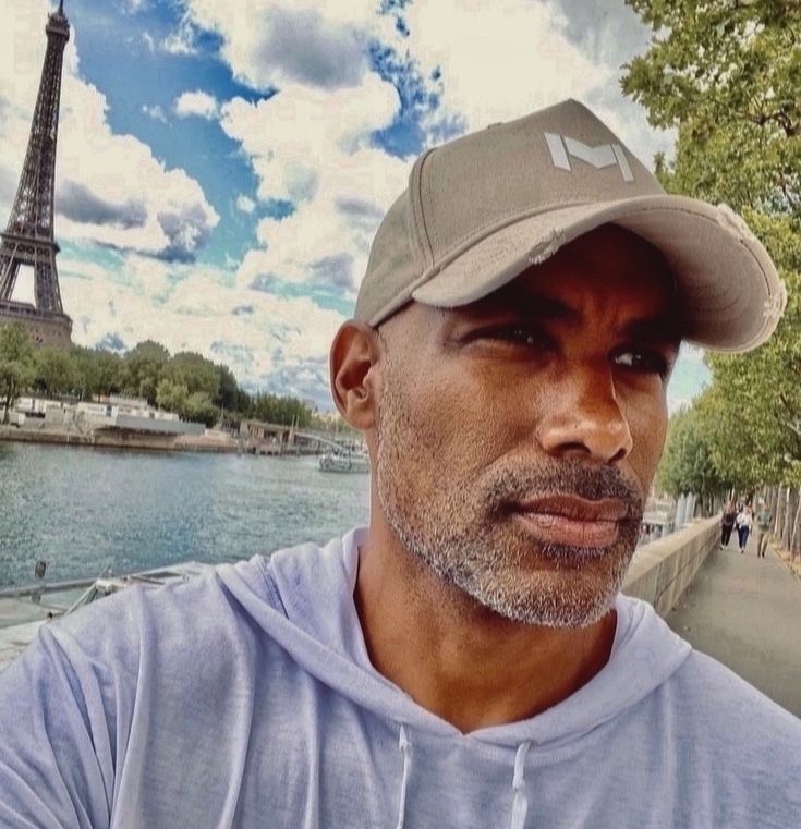 a man wearing a baseball cap in front of the eiffel tower, paris