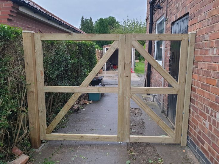 an open wooden gate on the side of a building next to a brick wall and bushes