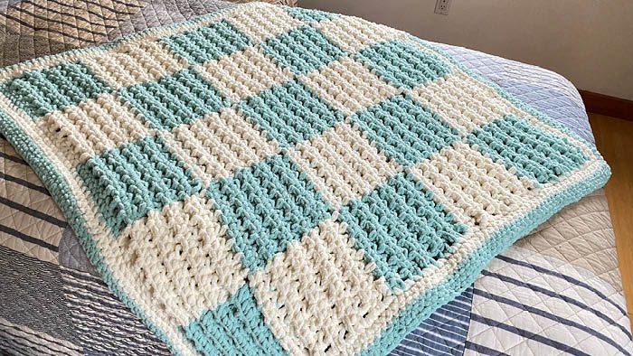 a crocheted blanket sitting on top of a bed next to pillows and blankets