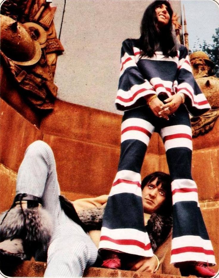 a woman in striped pants standing on top of a statue with her legs spread out