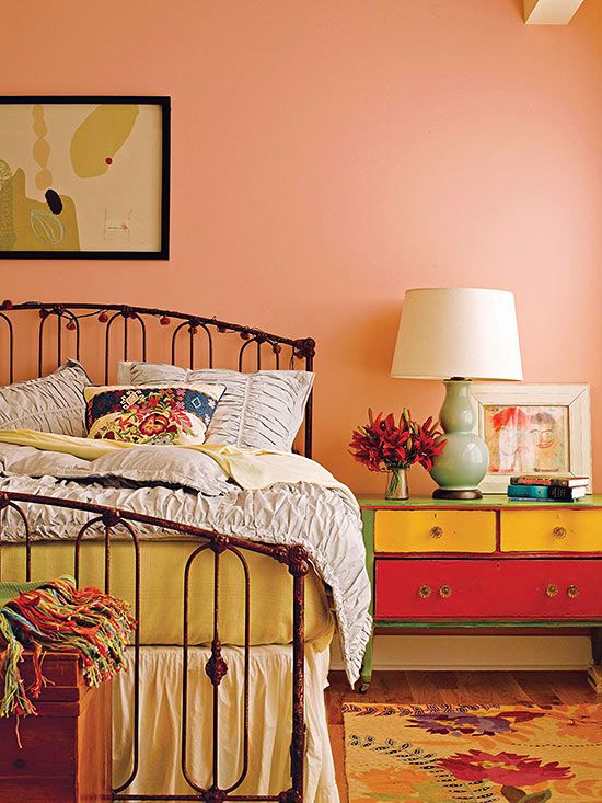 a bedroom with an iron bed frame and colorful dressers in the corner next to it