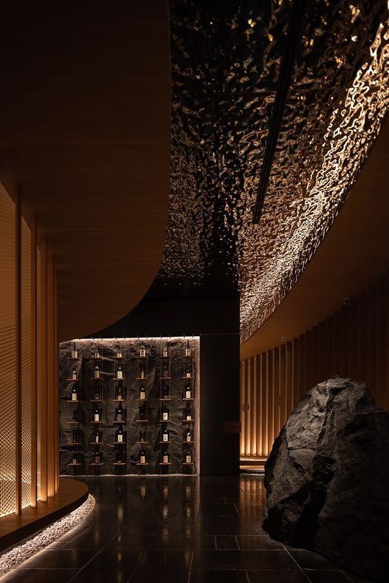 a large rock sitting in the middle of a room next to a wall filled with bottles