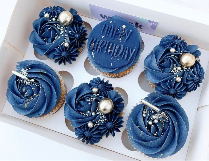 six cupcakes with blue frosting and pearls on them in a white box