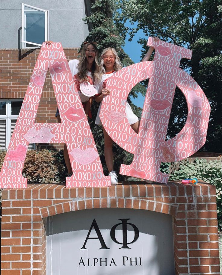 two women standing on top of a sign in front of a building