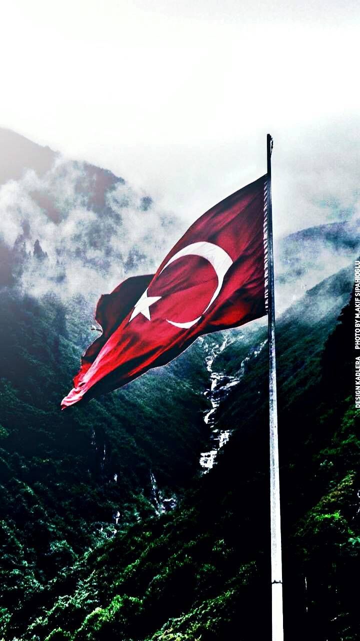 a flag flying in the wind on top of a lush green mountain covered in clouds