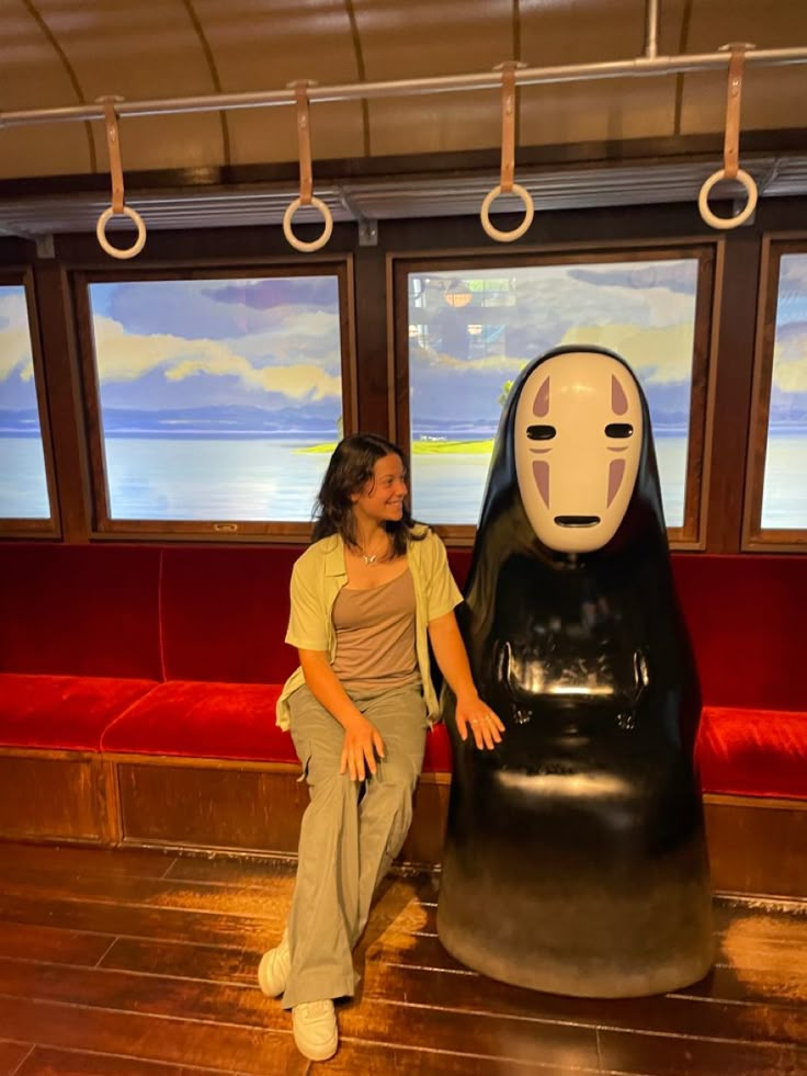 a woman sitting next to a statue in front of two windows with red seats behind her