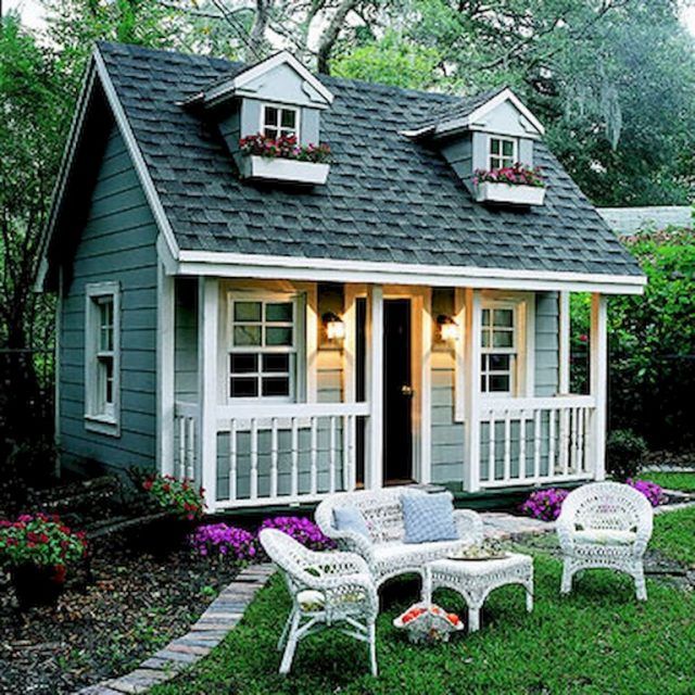 a small gray and white house with flowers on the windows, sitting in front of it