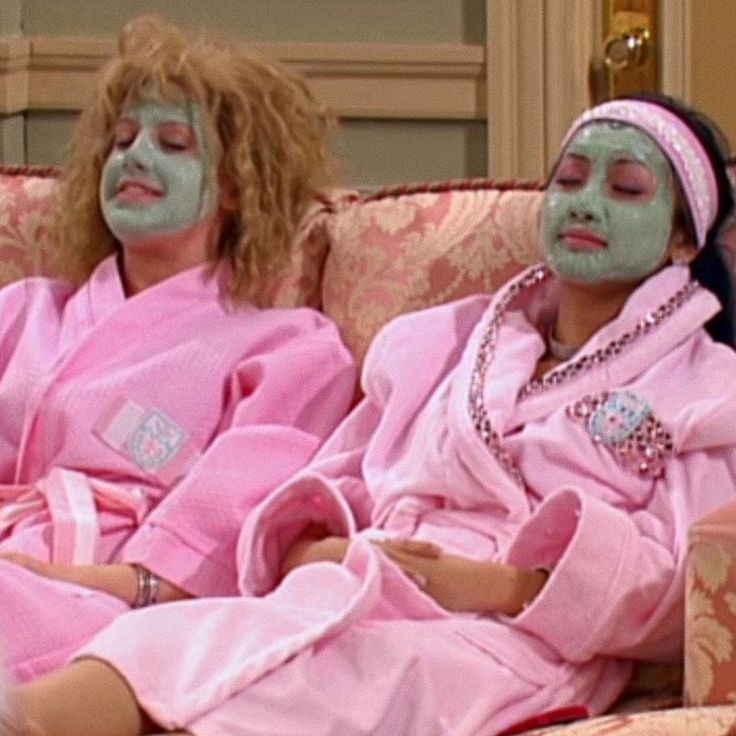 two women in pink robes sitting on a couch with their faces painted green and white