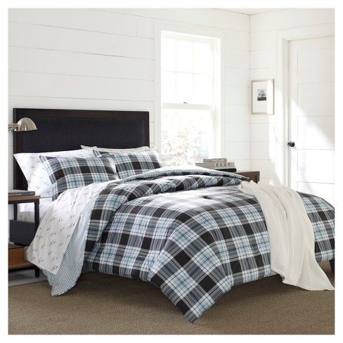 a bed with plaid comforter and pillows in a white room next to a window