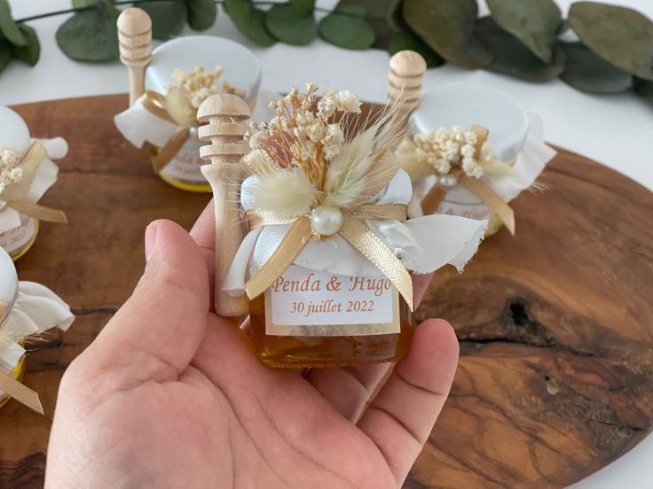 a hand holding a jar of honey with flowers on it and ribbon around the bottle