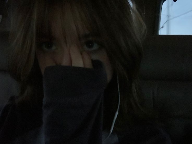 a woman covering her face in the back seat of a car with headphones on